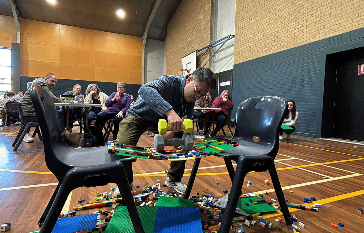 Large group of school staff participating in a Brick Masters challenge inside a school hall in Canberra.